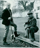 A hunter watches as a Eurasian lynx walks across a snow-covered field in Piz Sesvenna National Park, South Tyrol, Italy. - Vintage Photograph