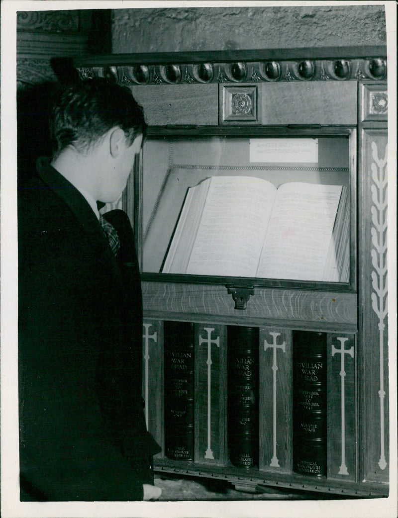 A man examines one of the four specially bound volumes containing the names of nearly 60,000 civilians killed by enemy action in the United Kingdom, placed in a shrine designed by Sir Charles Peers in Westminster Abbey. - Vintage Photograph