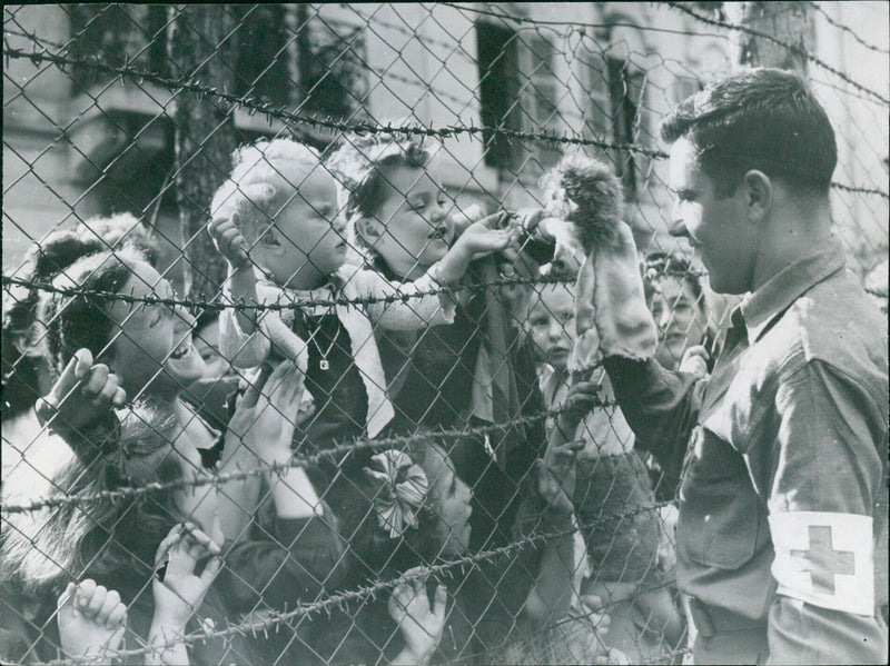 A US Army medical corpsman brings joy to children at the Vittel internment camp in France in 1944. - Vintage Photograph