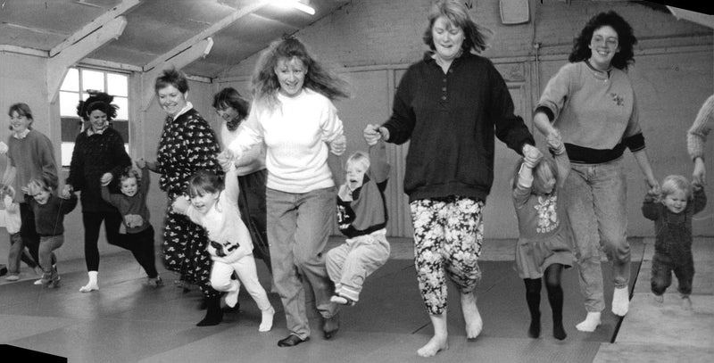 Energetic toddlers swing into action with their mothers at a music and movement session. - Vintage Photograph
