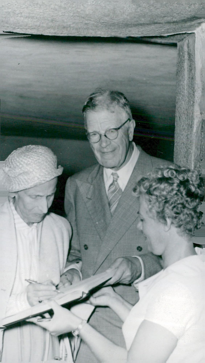 King Gustaf VI Adolf and Queen Louise write their signature in the guestbook that Brita HultÃ©n holds. - Vintage Photograph