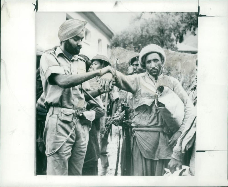 AN INDIAN SOLDIER CLAMPING A CHAIN ON THE ARM OF A PRISONER. - Vintage Photograph