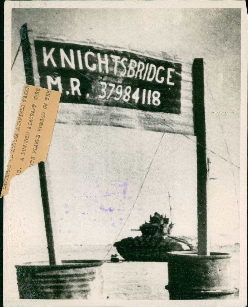 A heavy British tank passes behind the sign. - Vintage Photograph