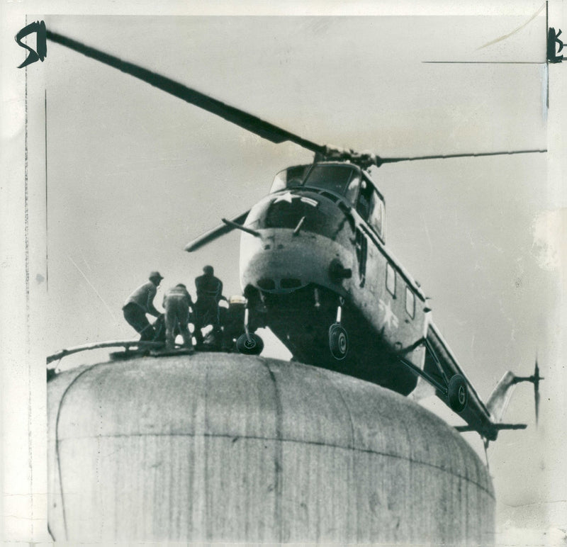 A UNITED STATES Army helicopter rests with one wheel on top of a water tower at Mount St. Joseph- on-the-Ohio College. - Vintage Photograph