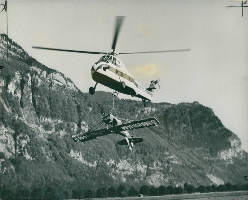 A helicopter lifting one of two light planes. - Vintage Photograph