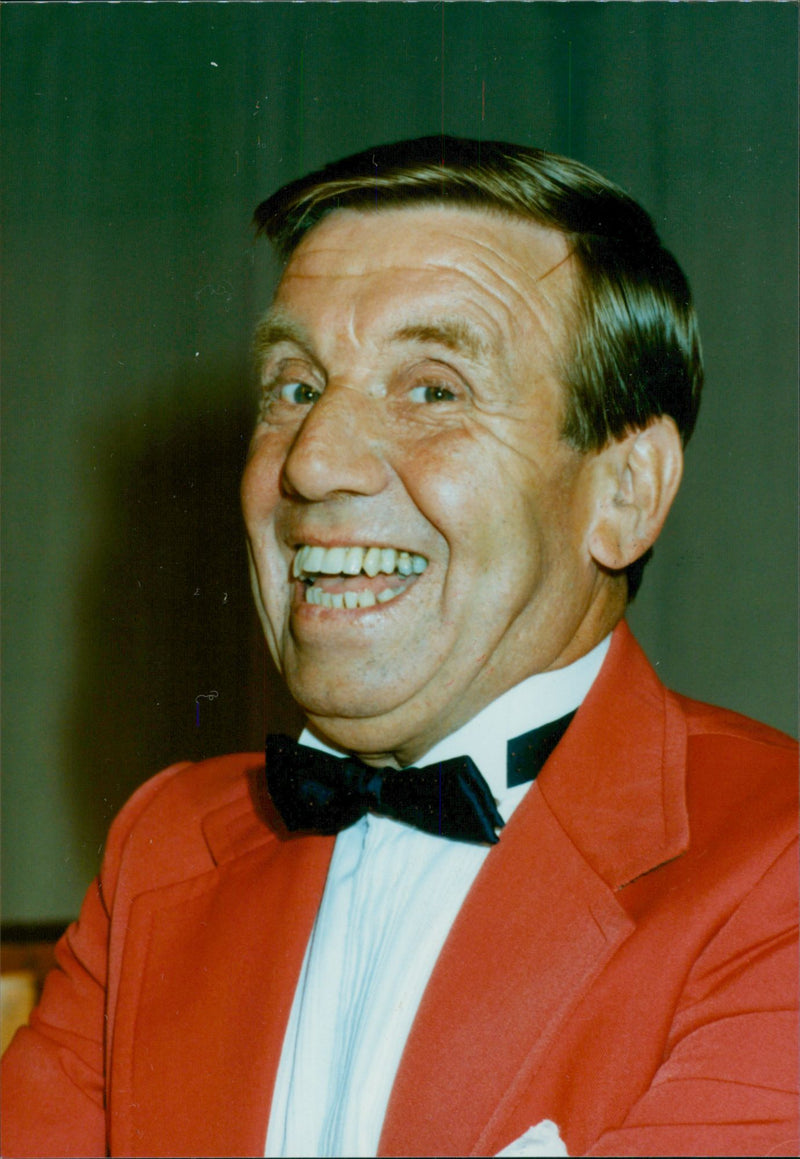 Johnny Hackett in his red suit with a wide smile on his face. - Vintage Photograph