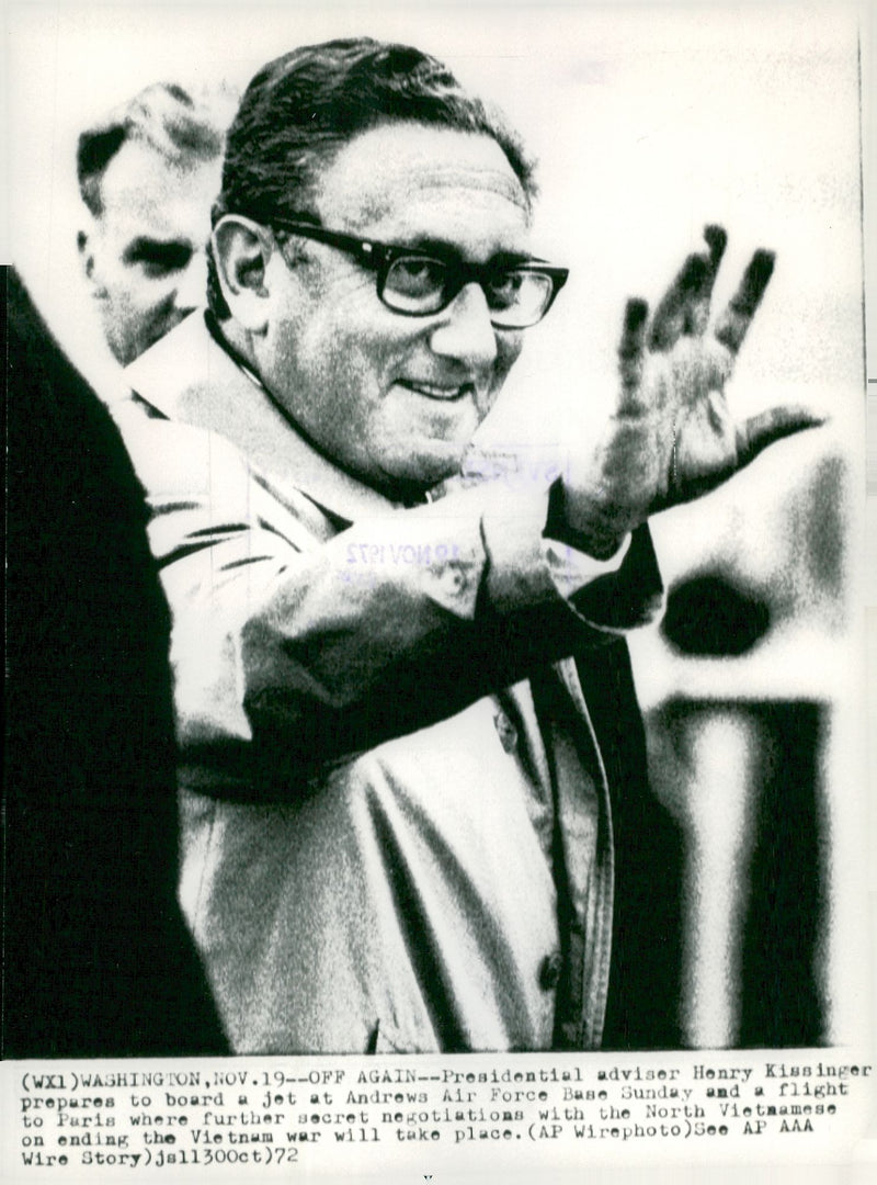 Henry Kissinger raises a hand in greetings as he board the planet to bring him to the end of the Vietnam War negotiations - Vintage Photograph