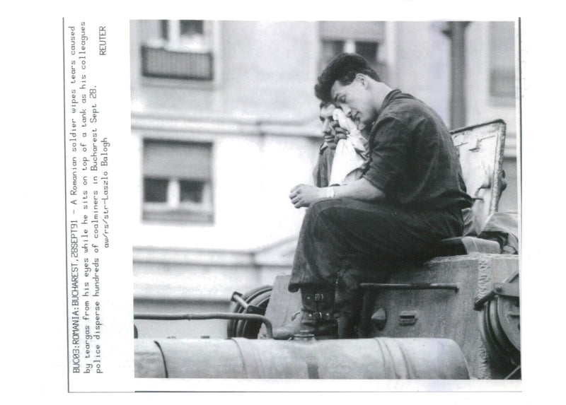 A romanian soldier wipes tears caused by teargas from his eyes while he sits on top of a tank. - Vintage Photograph