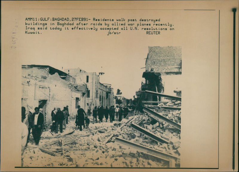 Residents walk past destroyed buildings in baghdad after raids by allied war planes recently. - Vintage Photograph