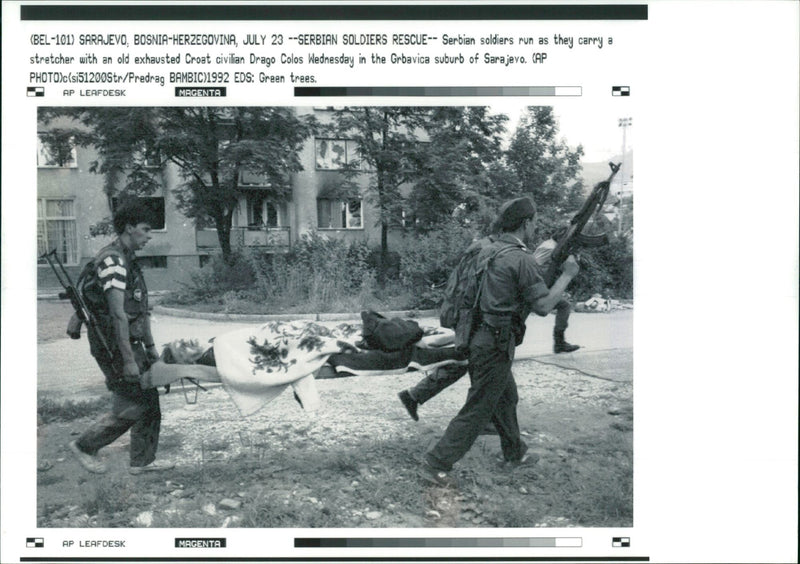 Serb soldiers run as they carry a stretcher. - Vintage Photograph