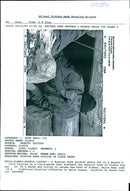 A Bosnian Serb soldier peers out of a dugout while talking on a field-phone. - Vintage Photograph