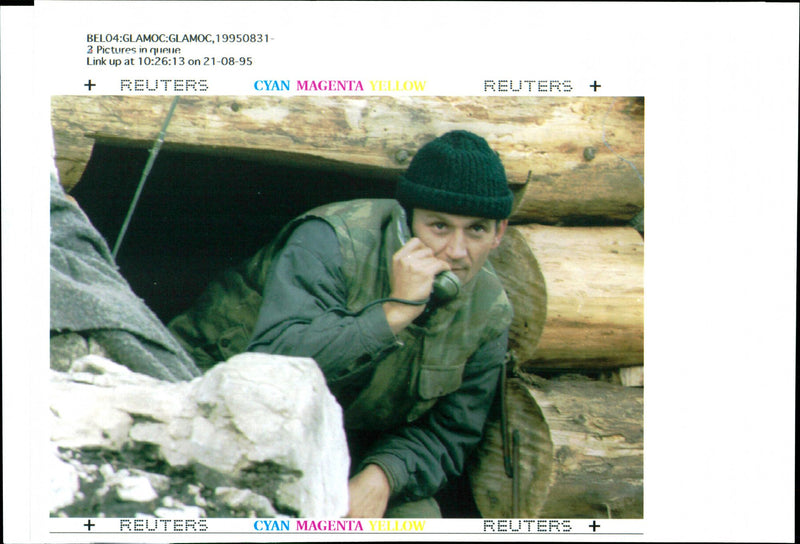 A Bosnian Serb soldier peers out of a dugout while talking on a field-phone. - Vintage Photograph
