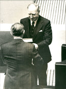 Minister of Justice Romaus hands over his speech to Speaker Henry Allard during Parliament 1977. - Vintage Photograph
