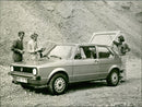 A group of people are looking at the Volkswagen Golf car. - Vintage Photograph