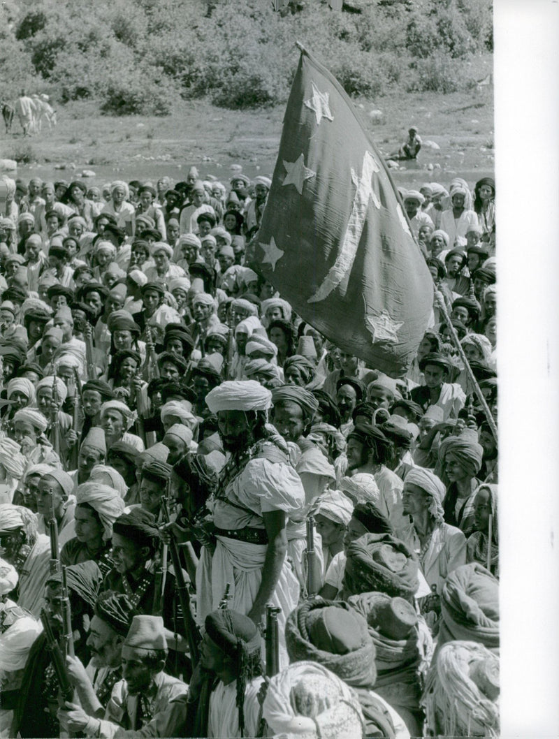 Warriors of Mutawakkilite Kingdom of Yemen have gathered in a place during North Yemen Civil War in 1962, they hold rifle and listening something - Vintage Photograph
