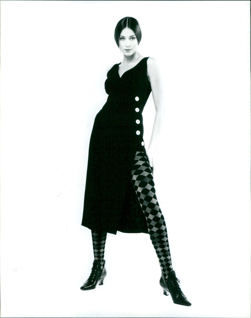 A model showcases a pair of harlequin-patterned opaque tights from Colture Designer Hosiery. - Vintage Photograph