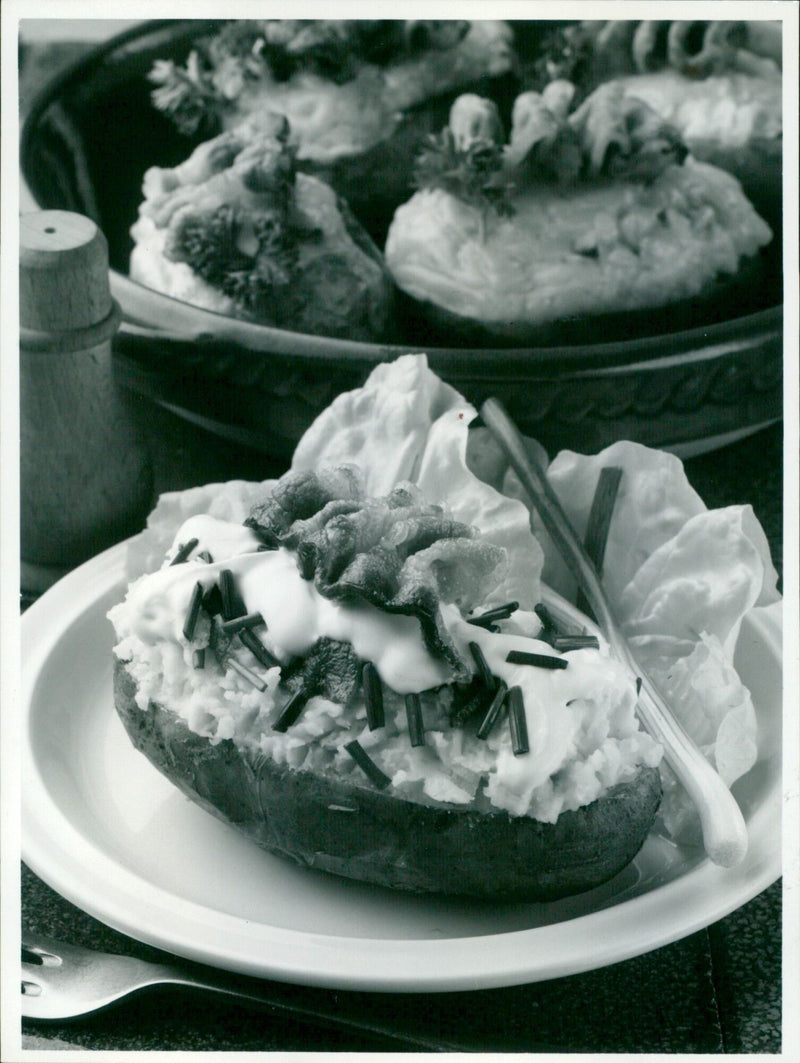 "A delicious baked potato garnished with chives, cream sauce, bacon, and spring onion." - Vintage Photograph