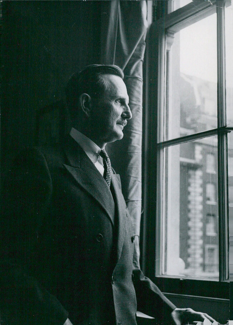 Mr. Julius C. Holmes, Charge d'Affaires of the American Embassy in London, is seen at the window of his office overlooking Grosvenor Square. - Vintage Photograph