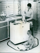 A father plays with a model train while his son looks on. - Vintage Photograph