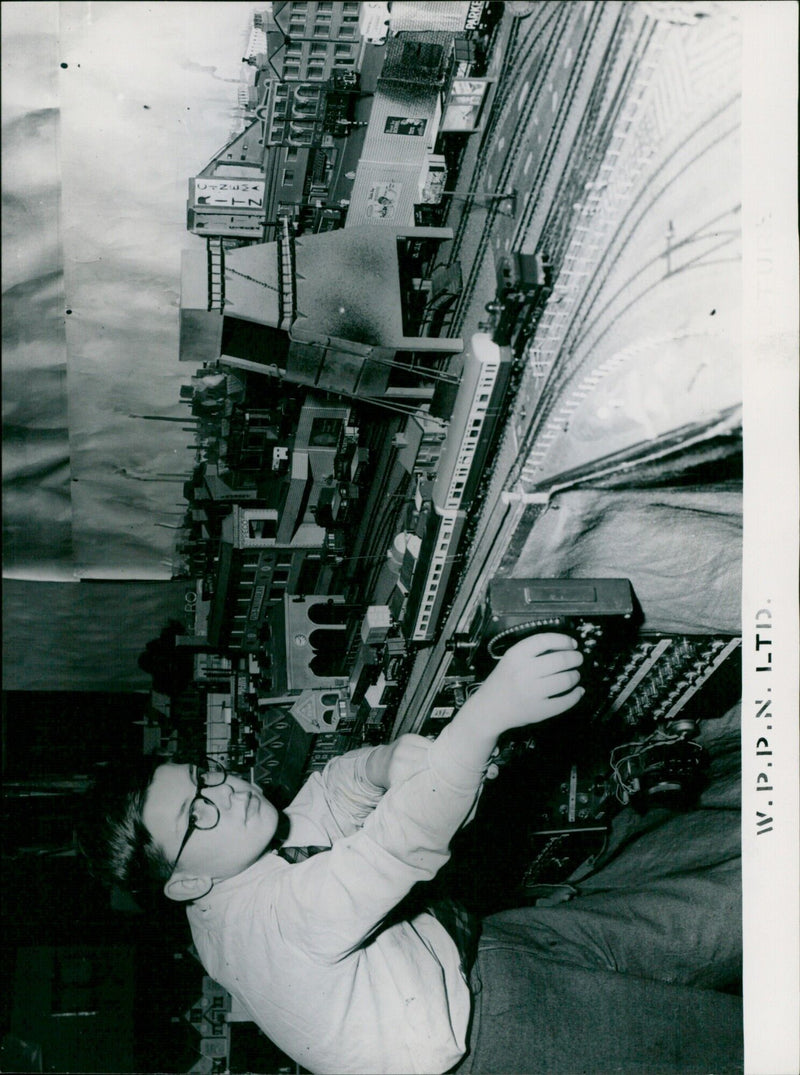 A young boy operates a model railway display depicting a British rail center. - Vintage Photograph