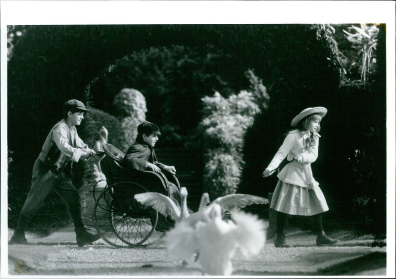 Three actors Andrew Knott, Heydon Prowse and Kate Haberly stand in a garden on the set of the 1993 British film, "The Secret Garden". - Vintage Photograph
