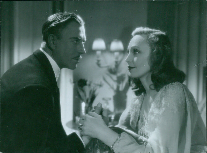 On August 8, 1943, a woman reads a copy of Hemmets Arsbok, a Swedish magazine, while the film "15 all Get brinner" plays in the background in Filey, Sweden. - Vintage Photograph