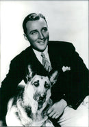 The iconic singer-songwriter Bing Crosby strikes a pose with his Alsatian dog in a 1974 photograph. - Vintage Photograph