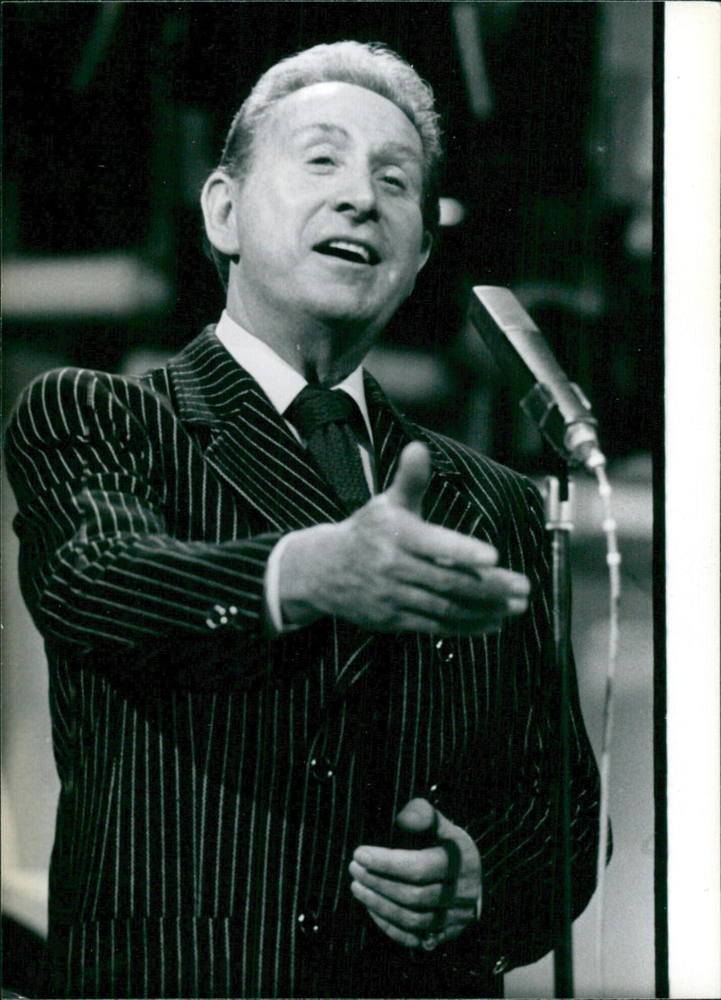 French singer and songwriter Charles Trenet performs on stage, accompanied by a live band. - Vintage Photograph