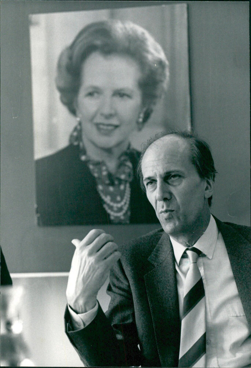 British Prime Minister Margaret Thatcher and Conservative Party Chairman Norman Tebbit are seen in a meeting beneath a portrait of Mrs. Thatcher, taken in 1987. - Vintage Photograph