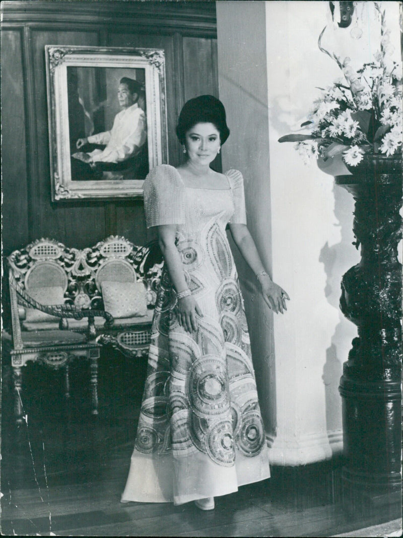 Mme. Imelda Marcos, First Lady of the Philippines, poses in front of a portrait of her husband, President Ferdinand Marcos. - Vintage Photograph