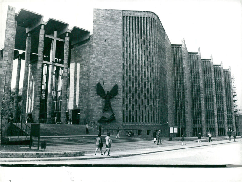 Visitors admire the bronze sculpture of St. Michael astride the Devil, created by Sir Jacob Epstein, on the north steps of Coventry Cathedral in London, England, UK. - Vintage Photograph