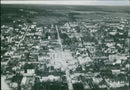 An aerial photograph taken in 1951 shows an airplane flying near the town of Herttstru 835 FDMR TIEK 1327, with the landscape below illuminated by the setting sun. - Vintage Photograph