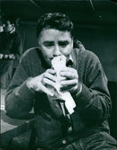In this picture taken in Sweden, a man is seen holding a movie camera while standing in front of a film set. - Vintage Photograph