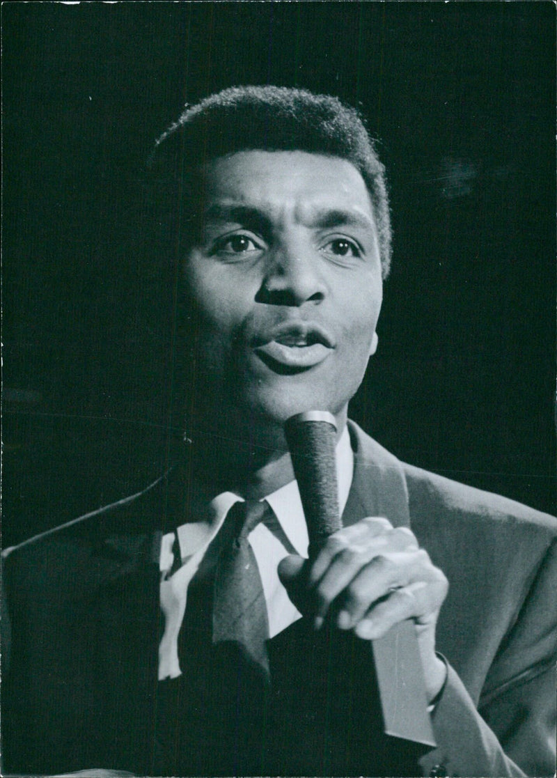 British pop singer Kenny Lynch performs at a London venue in 1963, with his hits "Mountain of Love," "Why Do You Treat Me Like This," "There's Never Been a Girl," and "Doll Face." - Vintage Photograph