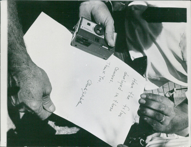 In this photograph, a man is seen holding an Instamatic F camera, ready to have the film developed. - Vintage Photograph