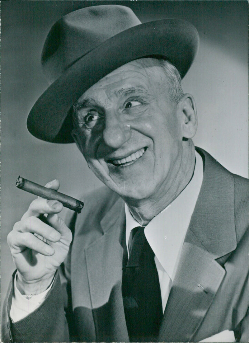 American entertainer Jimmy Durante is seen smiling and holding a microphone in London, England on 1092-32. - Vintage Photograph