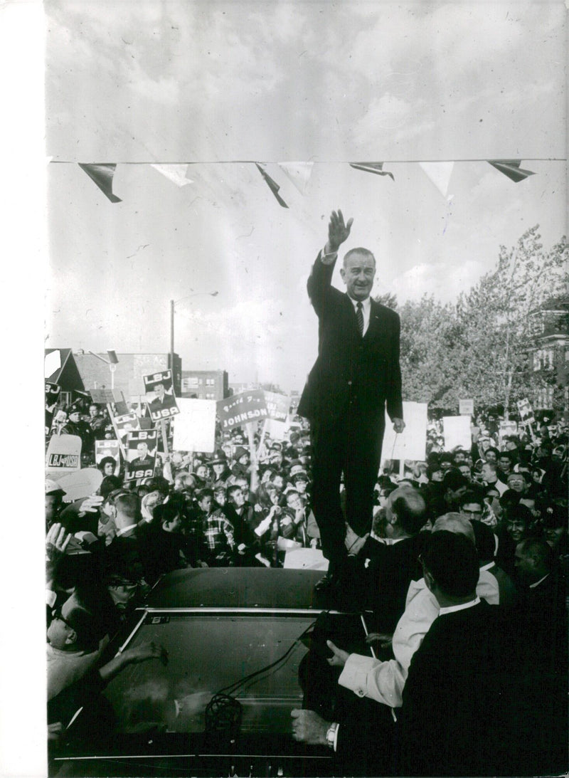 Vice President Lyndon B. Johnson, standing in front of a crowd of onlookers, waves to the camera in Torsgåt, Sweden on November 2, 1964. - Vintage Photograph