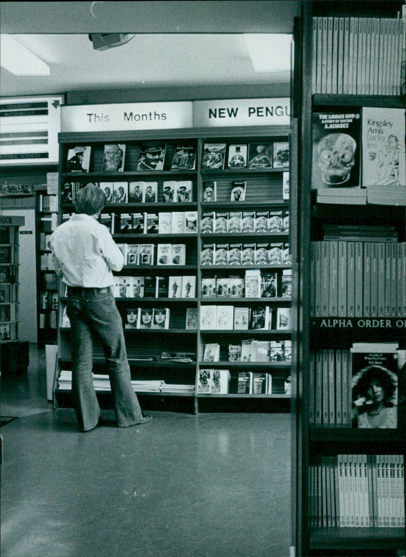 A man reads a selection of books in a bookstore. - Vintage Photograph