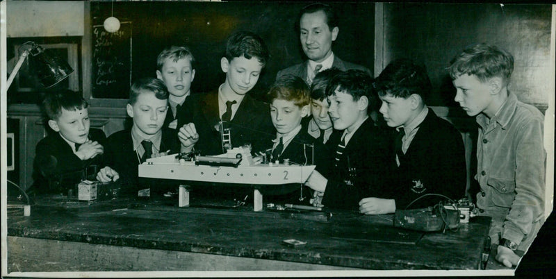 Boys of the Dragon School and their Science Master, Mr. G. Sommerhoff, demonstrate a model boat controlled by a remote radio. - Vintage Photograph