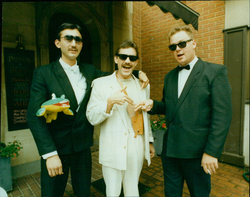 Police officers raid a cocktail bar in Oxford, England, only to find two men dressed in Miami Vice-style costumes with fake weapons. - Vintage Photograph