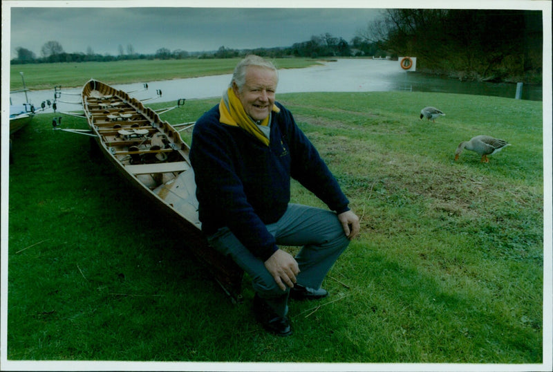 Geoffrey Beesley, boatman at St. Edward School, stands alongside the boat house dedicated to his parents. - Vintage Photograph