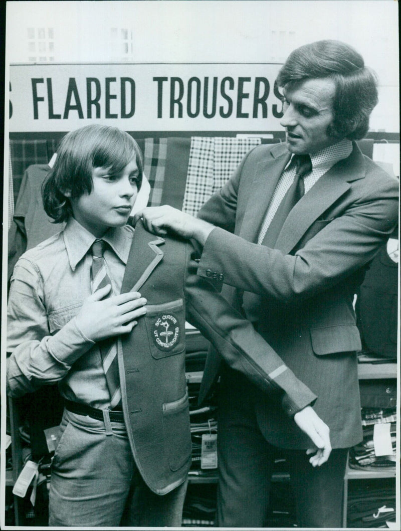 A young student wearing flared trousers and a back-to-school ad t-shirt walks down a street. - Vintage Photograph