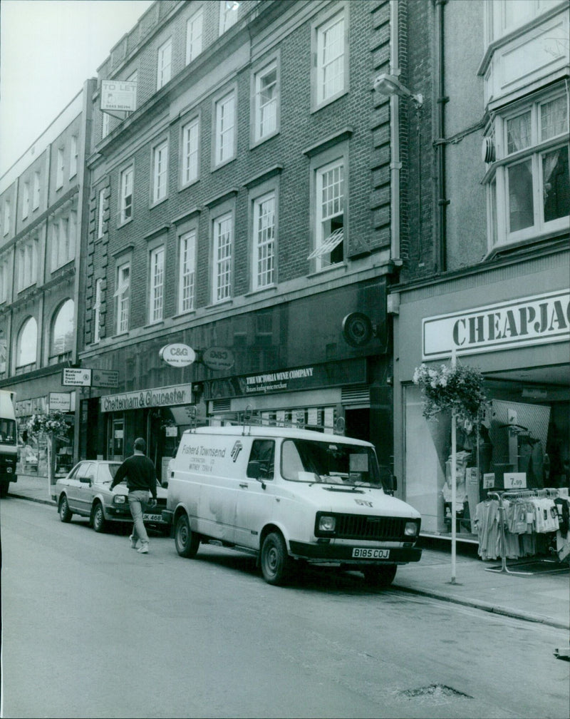 A group of people stand outside a bank, a building society, a wine shop, and other businesses. - Vintage Photograph