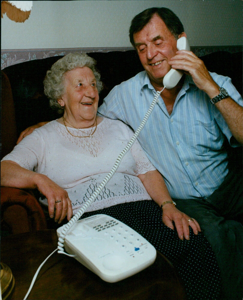 Ethel and John Simpson smile while holding a low telephone bill. - Vintage Photograph