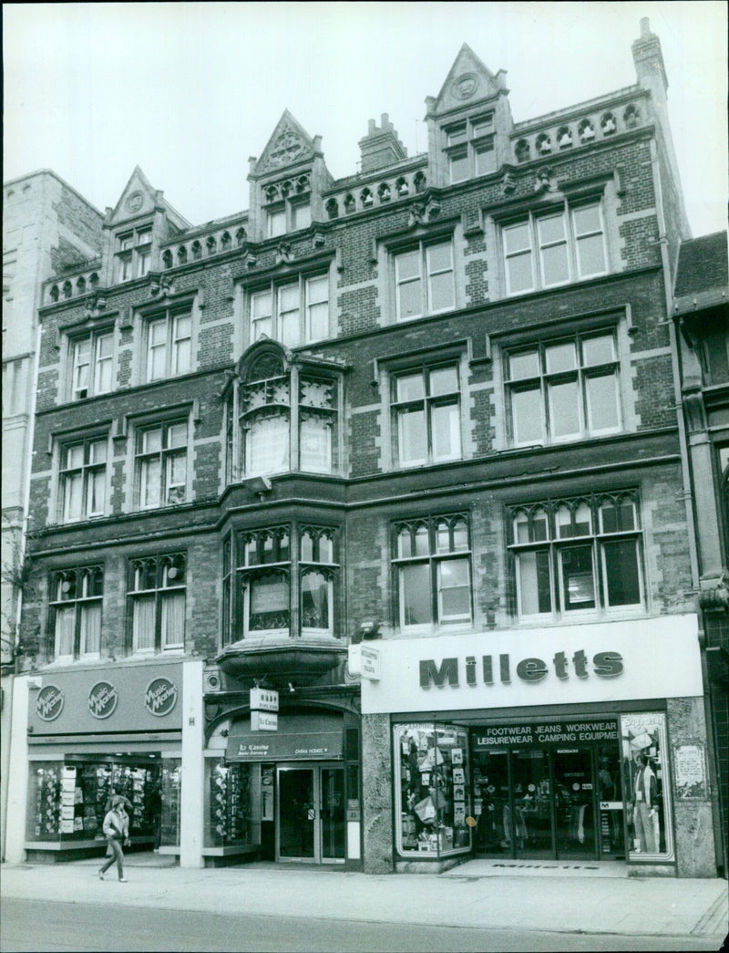 A woman wearing jeans, a Sish Music Destile t-shirt, and Milletts Footwear stands outside Chaudhry's in Oxford, UK. - Vintage Photograph