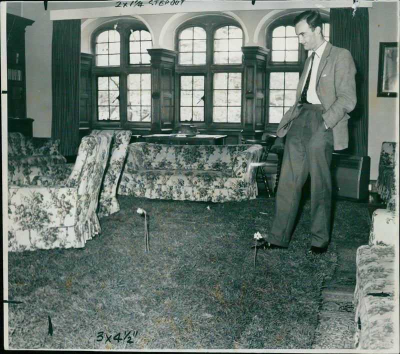 On May 8, 1953, Trinity College's Dean of Trinity, Mr. David S. Raven, manages a smile as he sees daffodils sprouting out of the Junior Common Room carpet, courtesy of Balliol College undergraduates. - Vintage Photograph