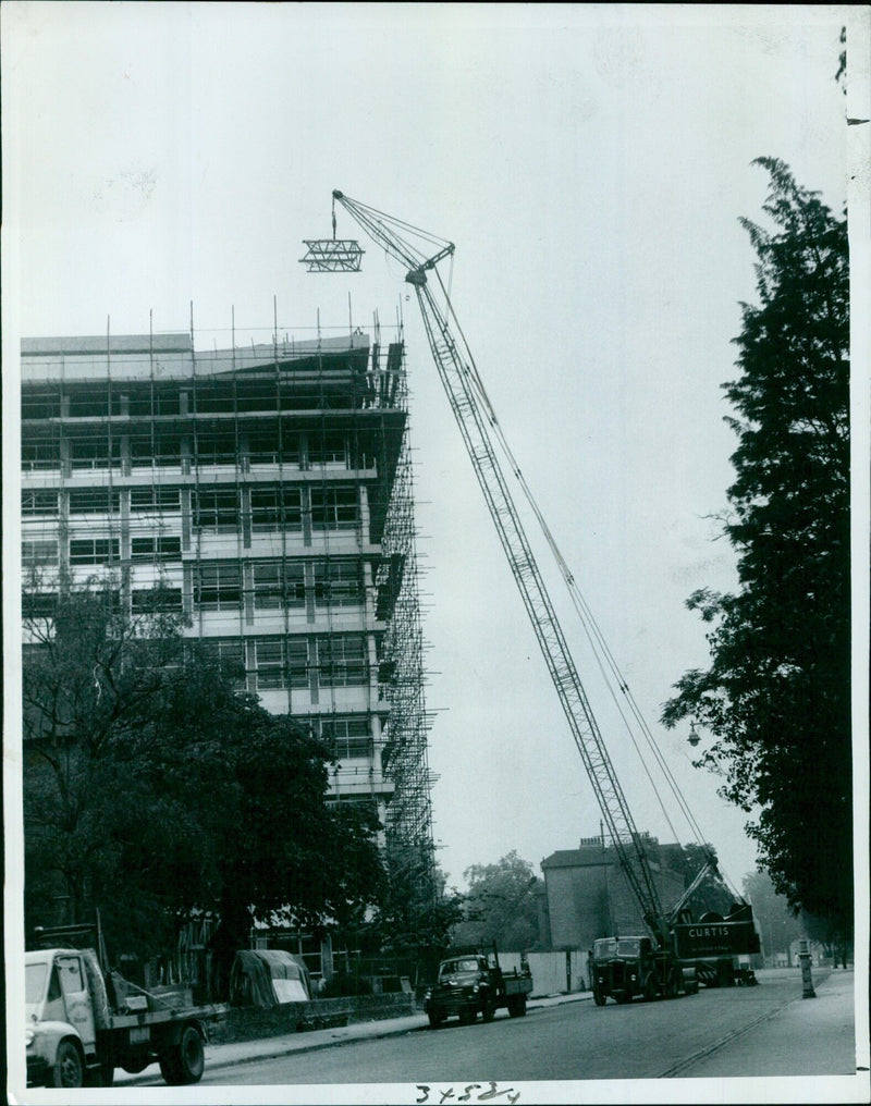 A mobile crane lifts sections of a tower crane from the roof of a construction site in Oxterd, England. - Vintage Photograph