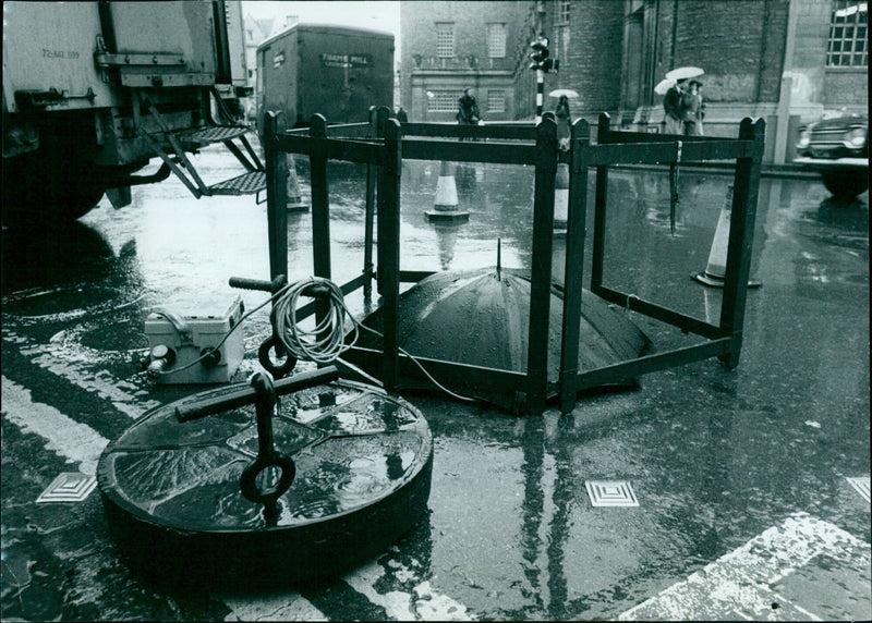 A Post Office Engineer stands on a manhole cover in Oxford, England, to keep his feet dry while working on cable junctions. - Vintage Photograph