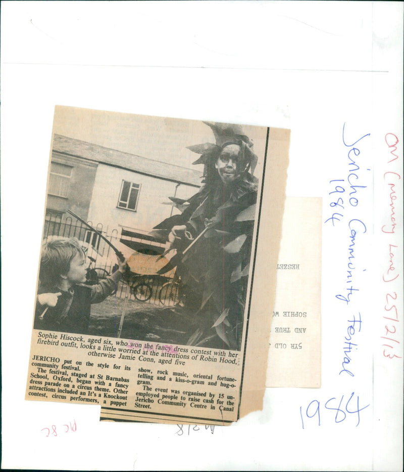 A six-year-old girl dressed as a firebird looks worriedly at five-year-old Jamie Conn dressed as Robin Hood at the 1984 Jericho Community Festival in Oxford. - Vintage Photograph