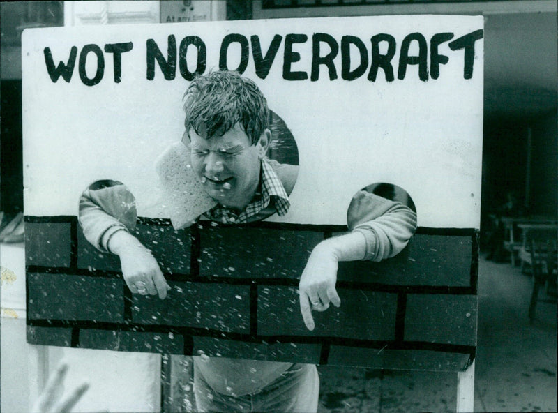 A woman stands in a crowded street, wearing a t-shirt with the words "WOT NO OVERDRAFT" printed on it. - Vintage Photograph